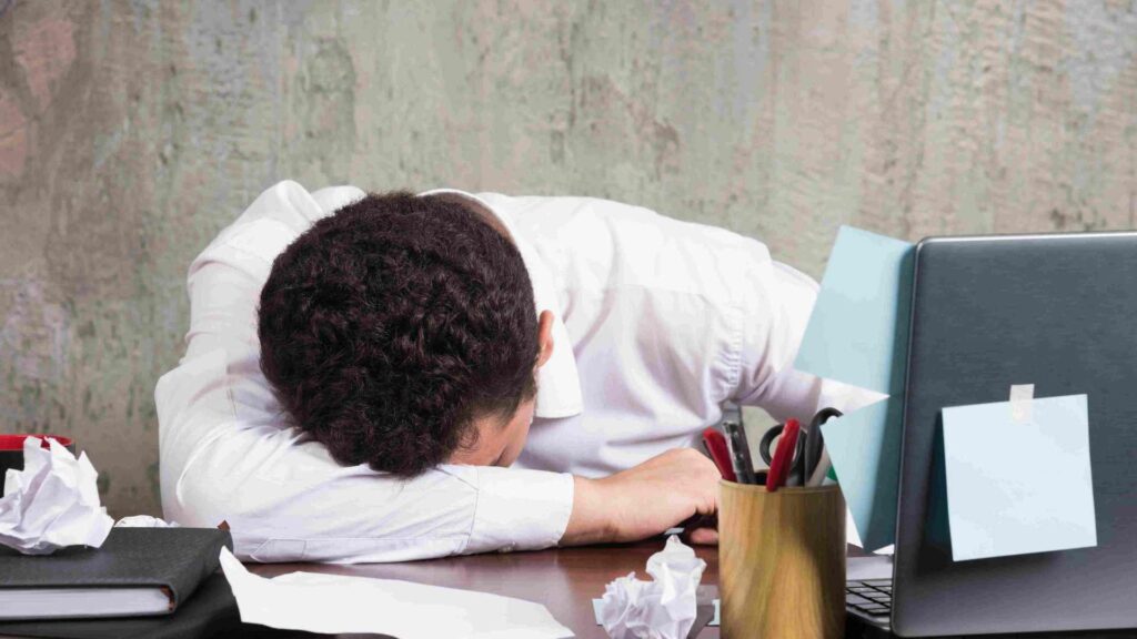 Seorang pekerja kantoran tertidur di meja kerja karena kelelahan setelah aktivitas padat seharian. Kondisi ini menggambarkan pentingnya Body Recovery pekerja kantoran untuk membantu tubuh kembali rileks dan menjaga produktivitas.
